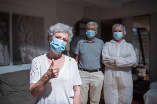 Free Senior woman gives thumbs up wearing mask with doctor and man in protective suits. Stock Photo