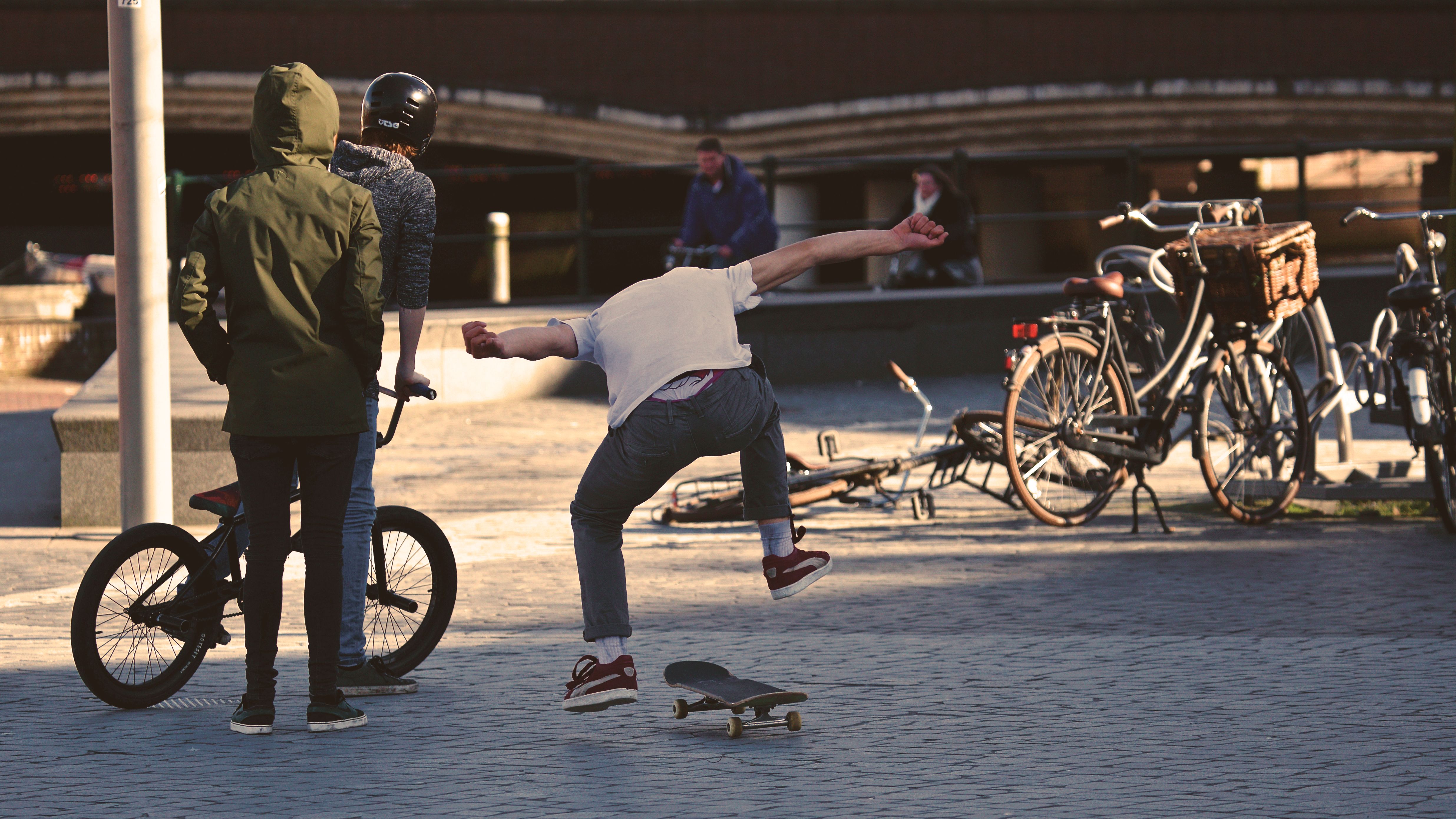 A vibrant city scene with young people skateboarding and biking in the summer sun.