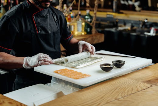 Chef in black uniform skillfully prepares sushi rolls with fresh salmon slices in a modern restaurant setting.