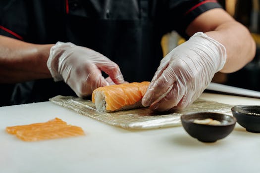 A close-up of a chef skillfully preparing a fresh salmon sushi roll in a restaurant kitchen.