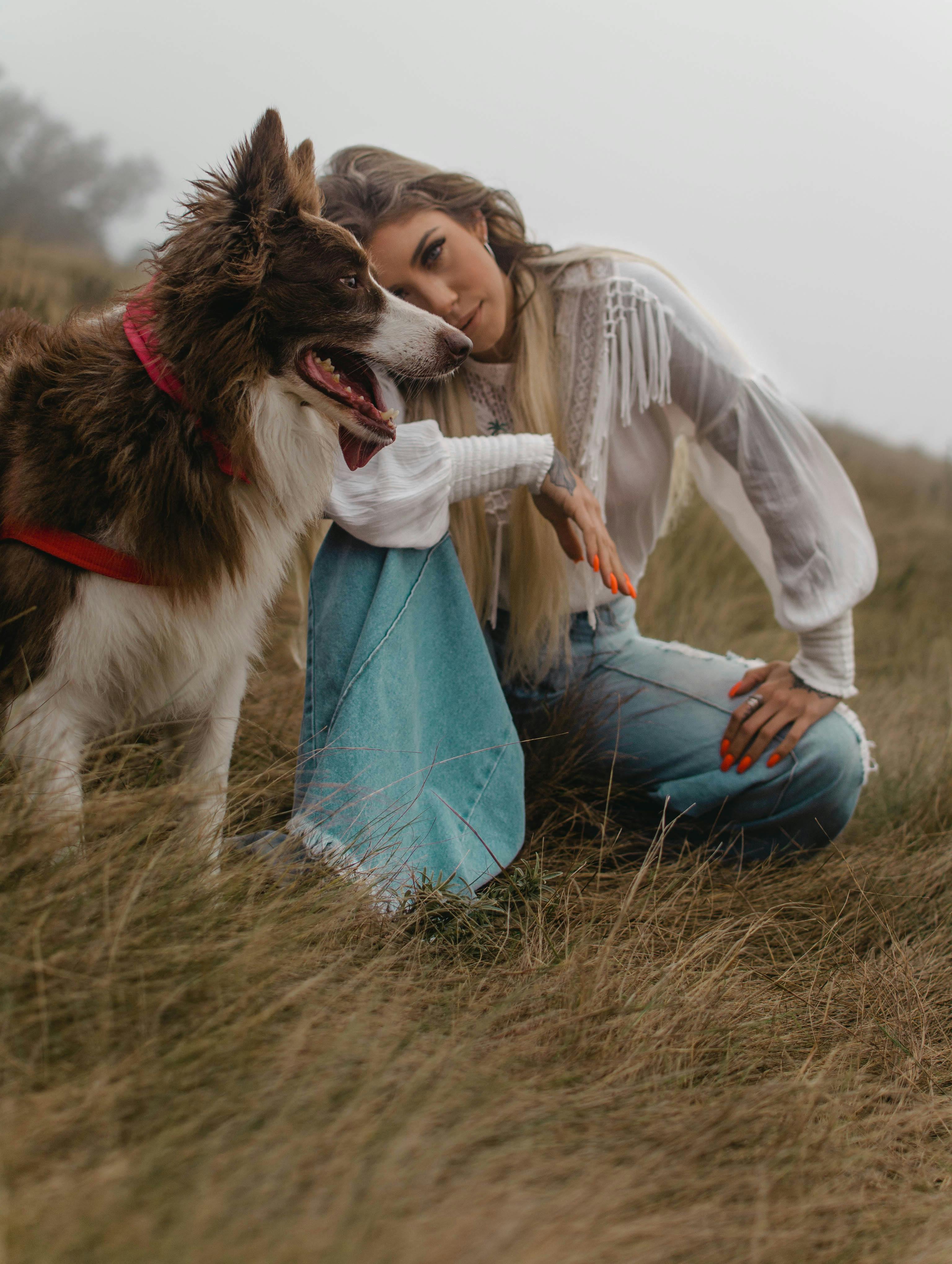 Woman kneeling beside her Border Collie in a scenic misty landscape.