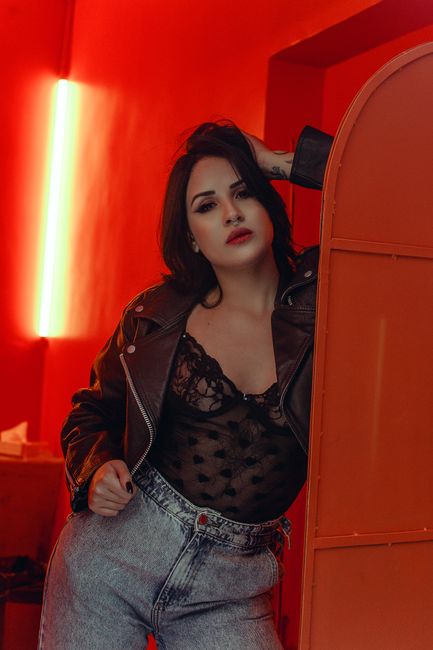 A fashionable woman posing indoors in a leather jacket and lace top.