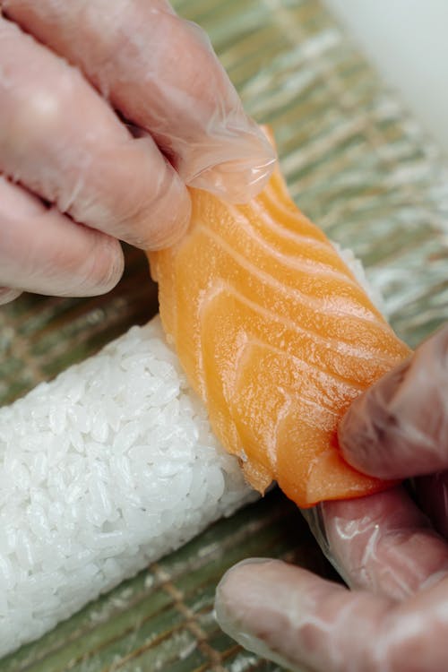 Person Making a Sushi Roll with Salmon