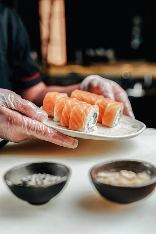 A Person with Gloves Holding a Plate of Salmon Sushi Rolls