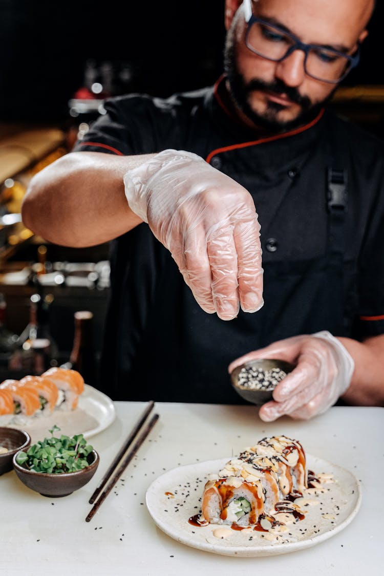 A Man Garnishing Sushi Rolls On A Plate