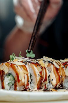 Close-up of a gourmet sushi roll garnished with almonds and sauce, shot indoors with a stylish minimalism.