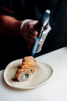 Chef using blowtorch to sear sushi rolls, highlighting delicious Japanese cuisine preparation.