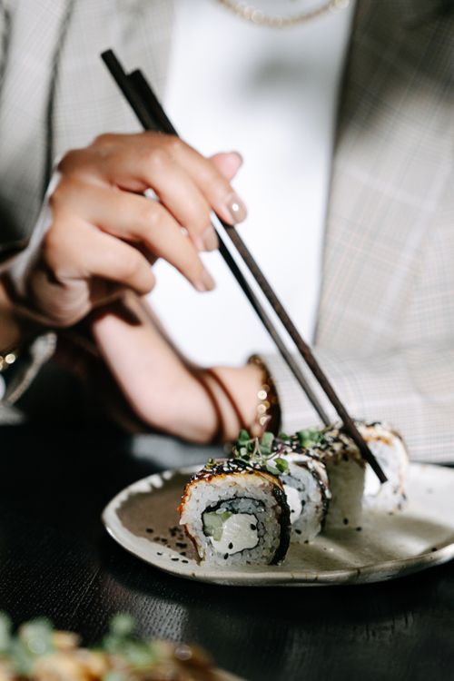 Free A detailed view of a hand using chopsticks to pick up sushi from a ceramic plate. Stock Photo