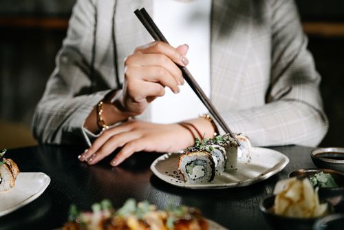 Free Close-up of a person enjoying sushi with chopsticks in a stylish restaurant setting. Stock Photo