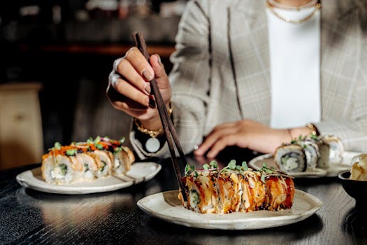 Woman using chopsticks to eat sushi roll with garnish on ceramic plate.