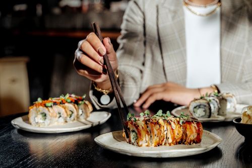 Free Woman using chopsticks to eat sushi roll with garnish on ceramic plate. Stock Photo