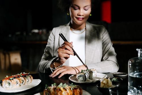 Free A woman dining indoors, enjoying sushi with chopsticks, creating an elegant and modern atmosphere. Stock Photo