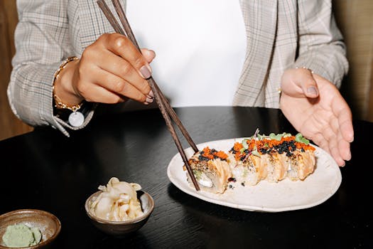 A woman in a blazer enjoys sushi rolls with chopsticks at a restaurant table.