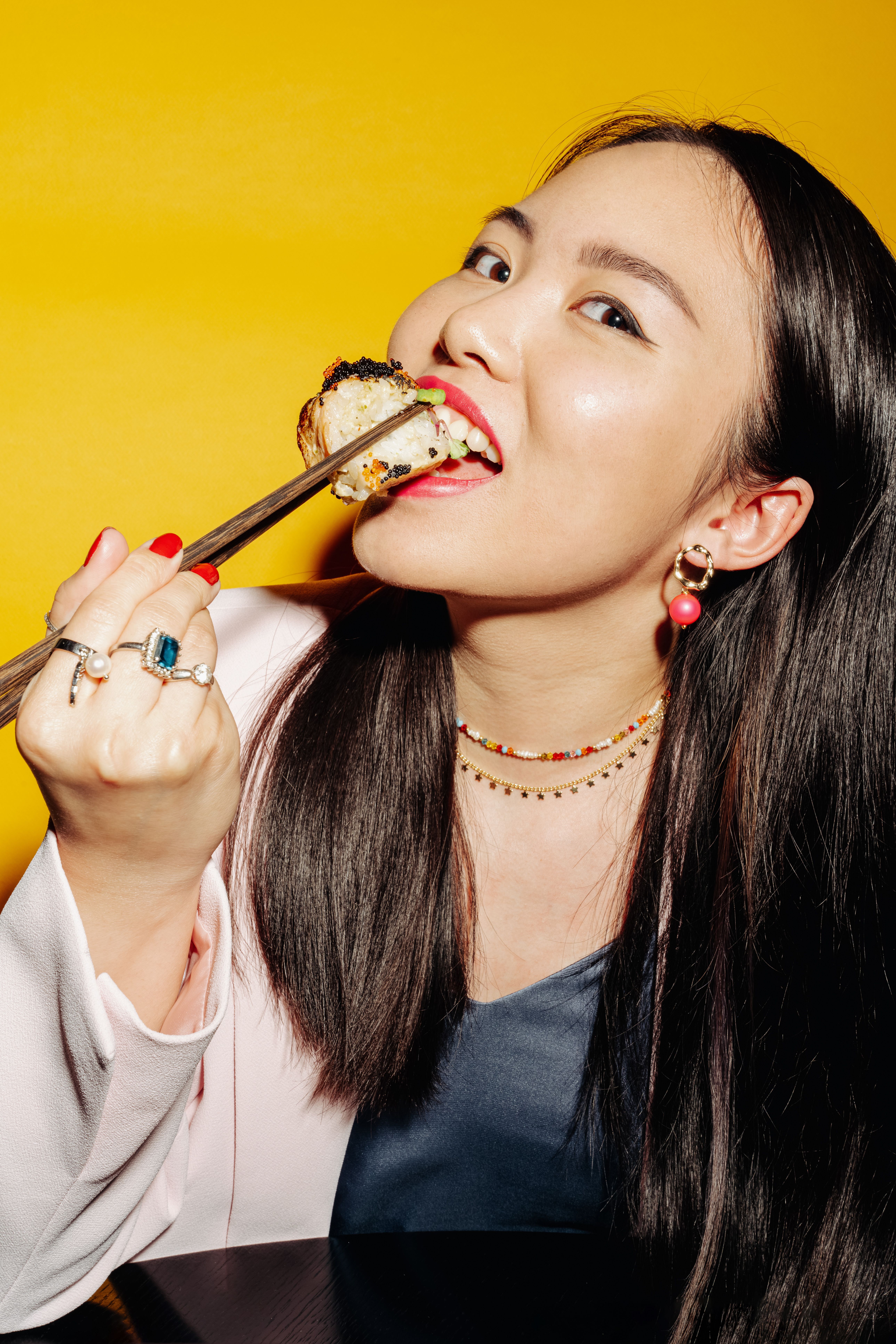 Close-up of joyful Asian woman enjoying sushi against a vibrant yellow background.
