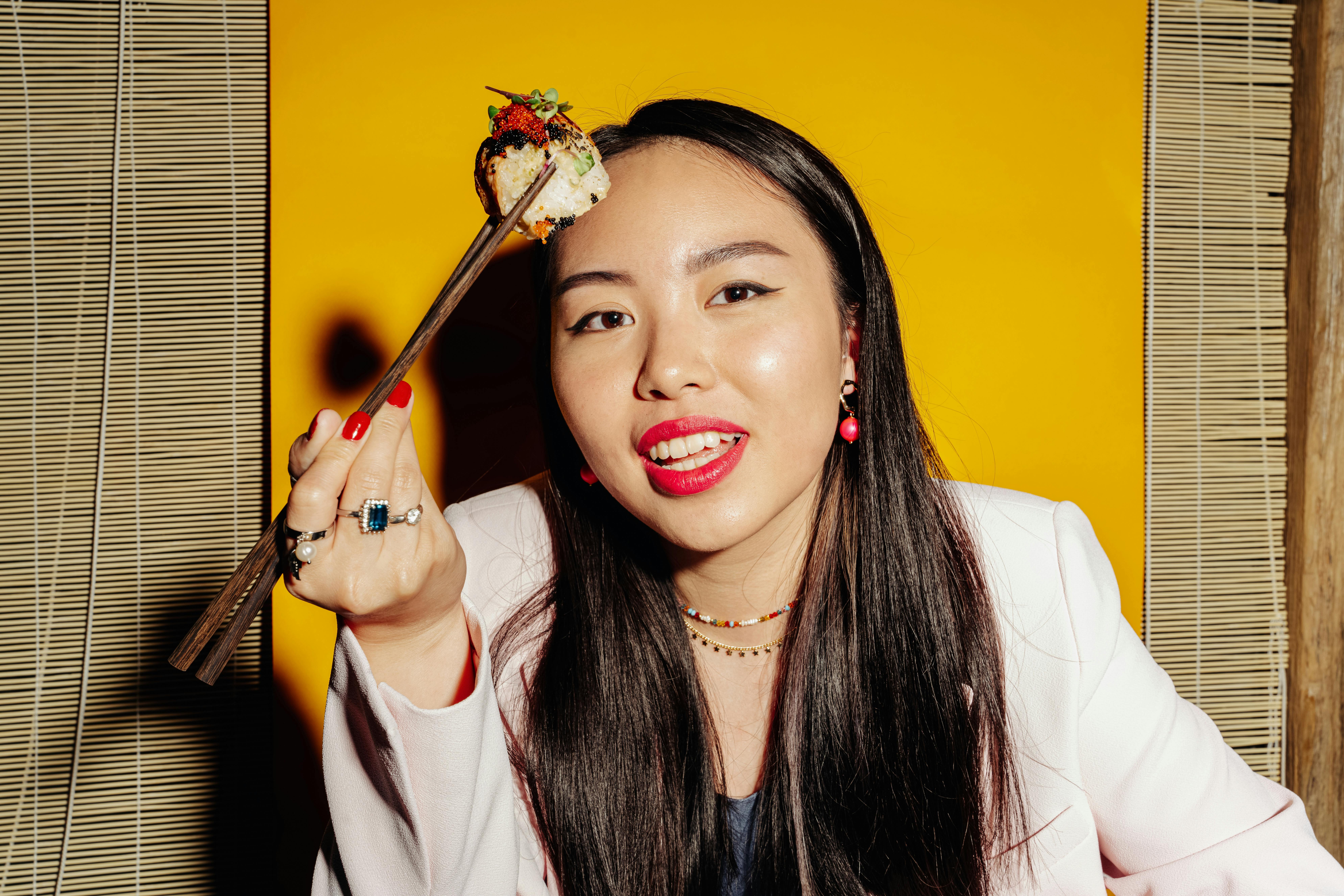 Vibrant portrait of a woman holding sushi with chopsticks against a bright yellow background.
