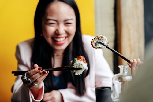 Free A joyful woman enjoying sushi with chopsticks in a vibrant setting. Stock Photo