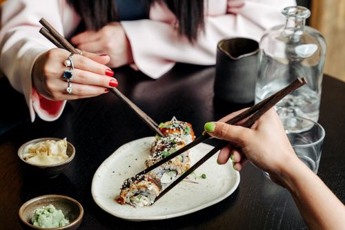 Free Two hands using chopsticks to enjoy sushi in a restaurant setting. Fresh and inviting Japanese cuisine. Stock Photo