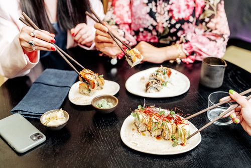 Free A group of people dining together, enjoying sushi with chopsticks and various condiments on a table. Stock Photo