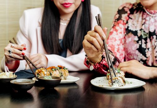 Free Two women enjoy sushi with chopsticks, showcasing a modern dining experience. Stock Photo