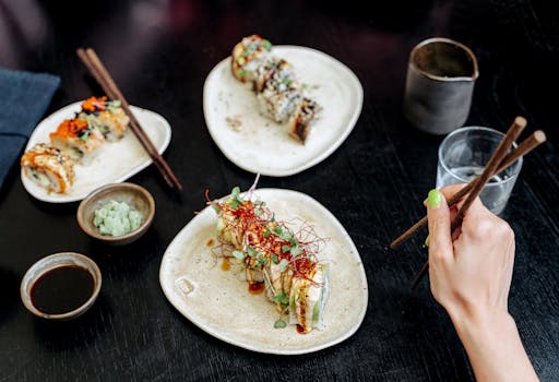 Close-up of assorted sushi rolls with chopsticks and dipping sauces on a dark table.