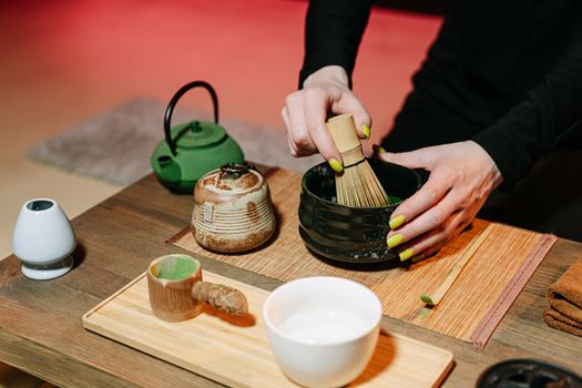 Close-up of hands preparing matcha in a traditional Japanese tea ceremony with utensils.
