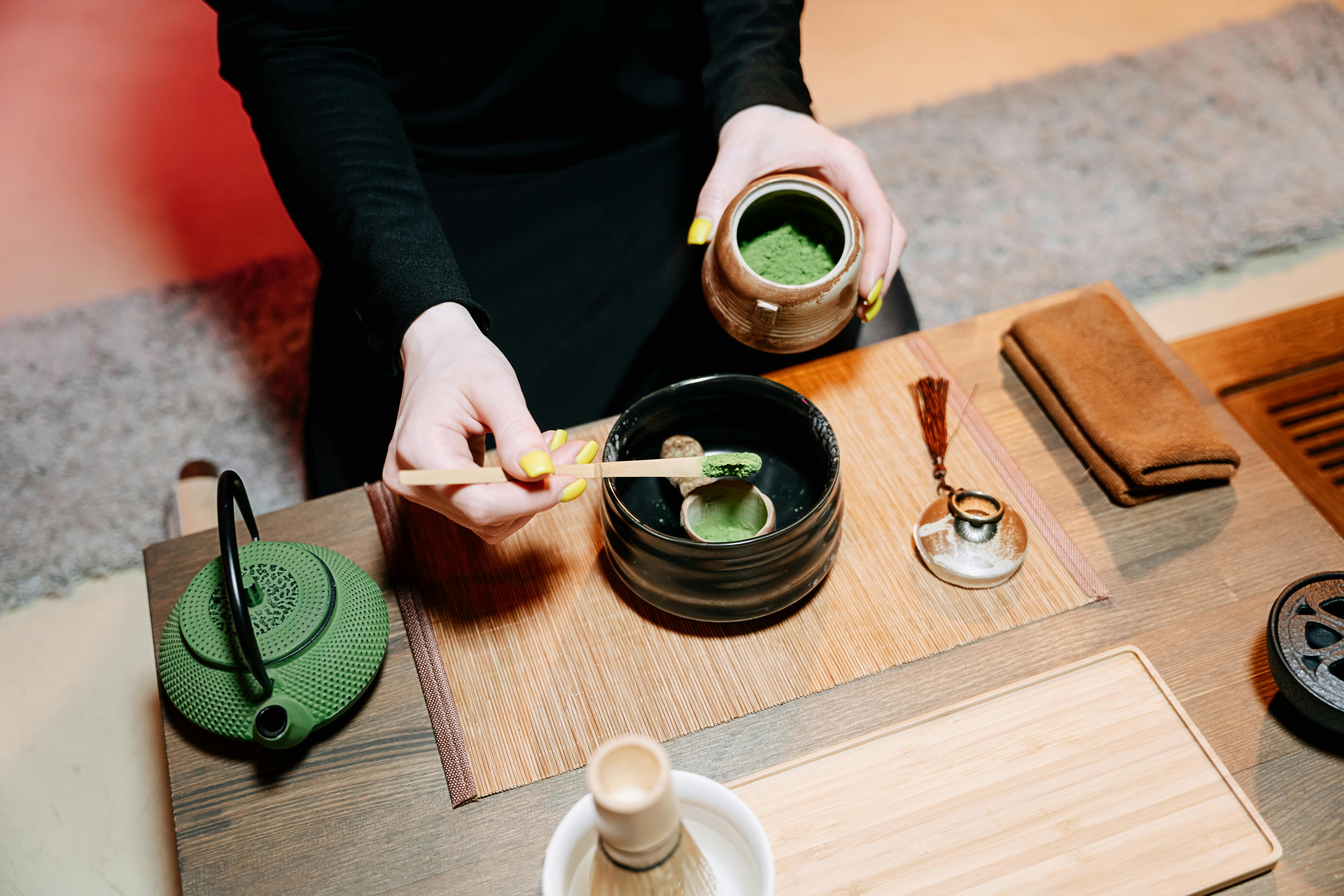 Hands preparing matcha tea in a traditional Japanese ceremony with vibrant green and earthy tones.