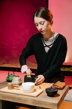 Elegant portrait of a woman preparing tea in a traditional ceremony with warm lighting.