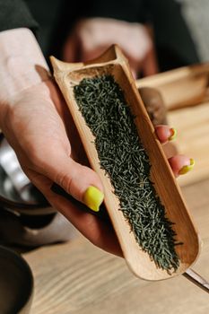 Hand holding bamboo scoop filled with dry green tea leaves during a traditional tea ceremony.