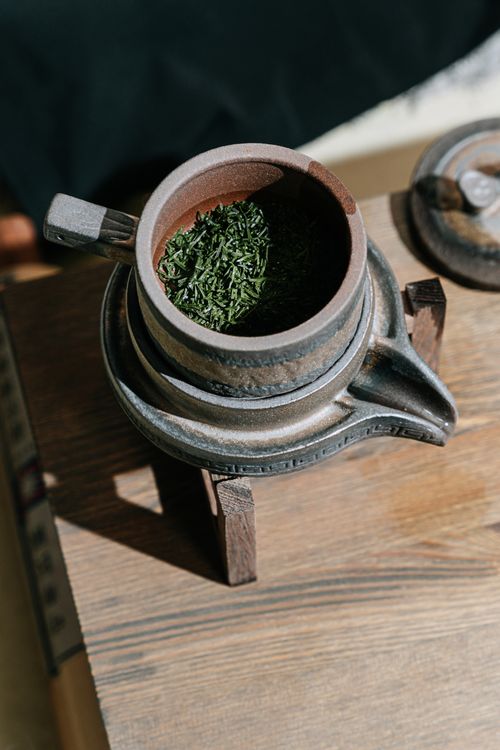 Free Close-up of a ceramic teapot with green tea leaves, perfect for a traditional tea ceremony. Stock Photo