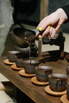 Close-up of a hand pouring tea into clay cups, showcasing traditional pottery and tea culture.