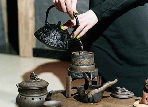 A woman pours hot water from a traditional teapot into a rustic cup during a tea ceremony.