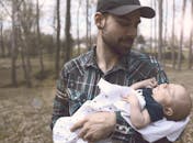 一位父亲在户外慈爱地抱着他刚出生的孩子，捕捉到了一个温柔的育儿时刻