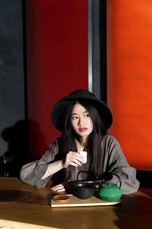 Free Elegant Asian woman in a black hat enjoying a traditional tea ceremony indoors. Stock Photo