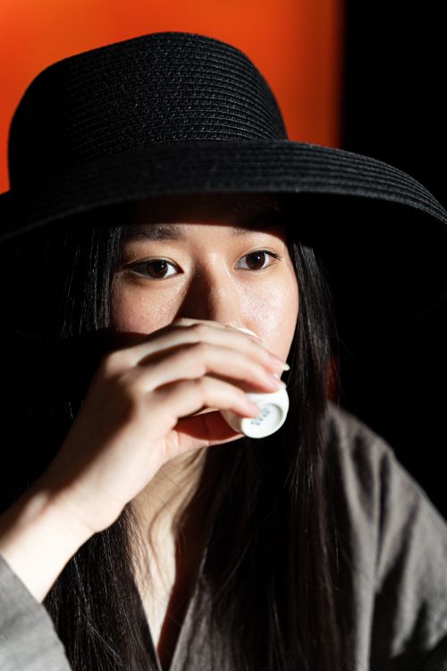 Free An Asian woman in a black hat enjoying a cup of tea, looking thoughtful. Stock Photo