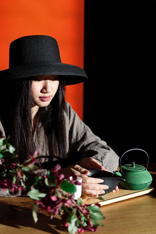 Free Asian woman wearing a hat enjoying a tea ceremony with a teapot and flowers in the setting. Stock Photo