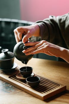 Close-up of a traditional tea ceremony pouring tea into cups on a wooden surface.