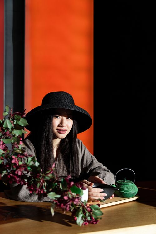 Free A woman in a black hat sitting at a table with a tea pot, surrounded by floral decor. Stock Photo