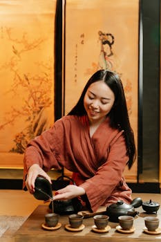 Asian woman in traditional attire pouring tea during an elegant tea ceremony indoors.