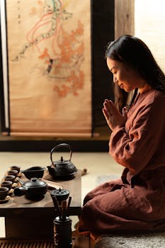 Asian woman performing a traditional tea ceremony indoors, kneeling in meditation.