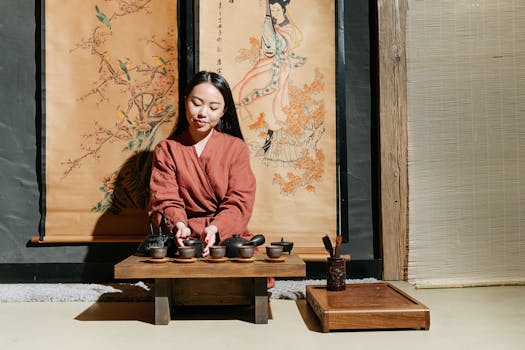 Asian woman performing traditional tea ceremony indoors with decorative scrolls.