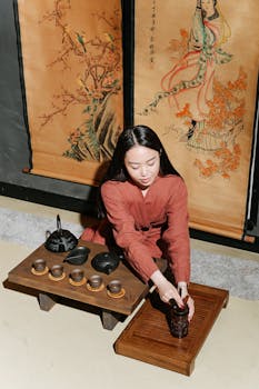 A woman performing a traditional tea ceremony with an elegant setup and oriental decor.