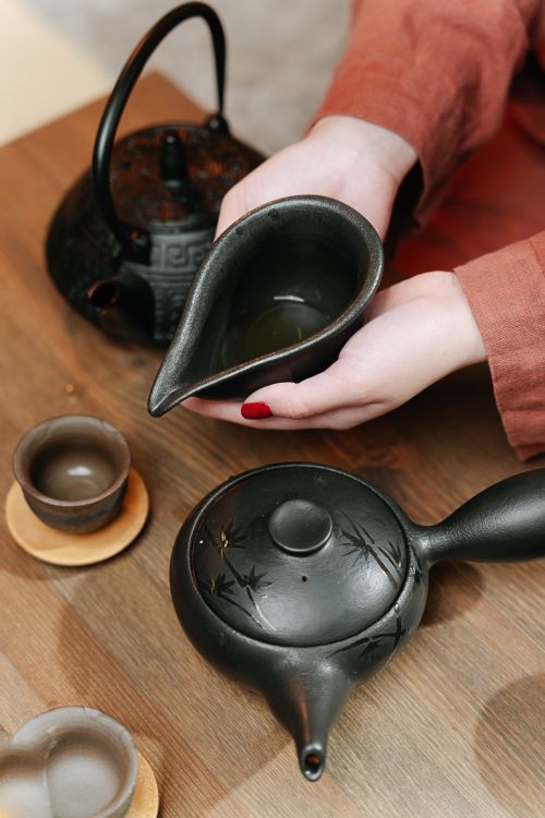 Free Hands holding a teapot during a traditional tea ceremony, featuring ceramic tea set on wooden table. Stock Photo