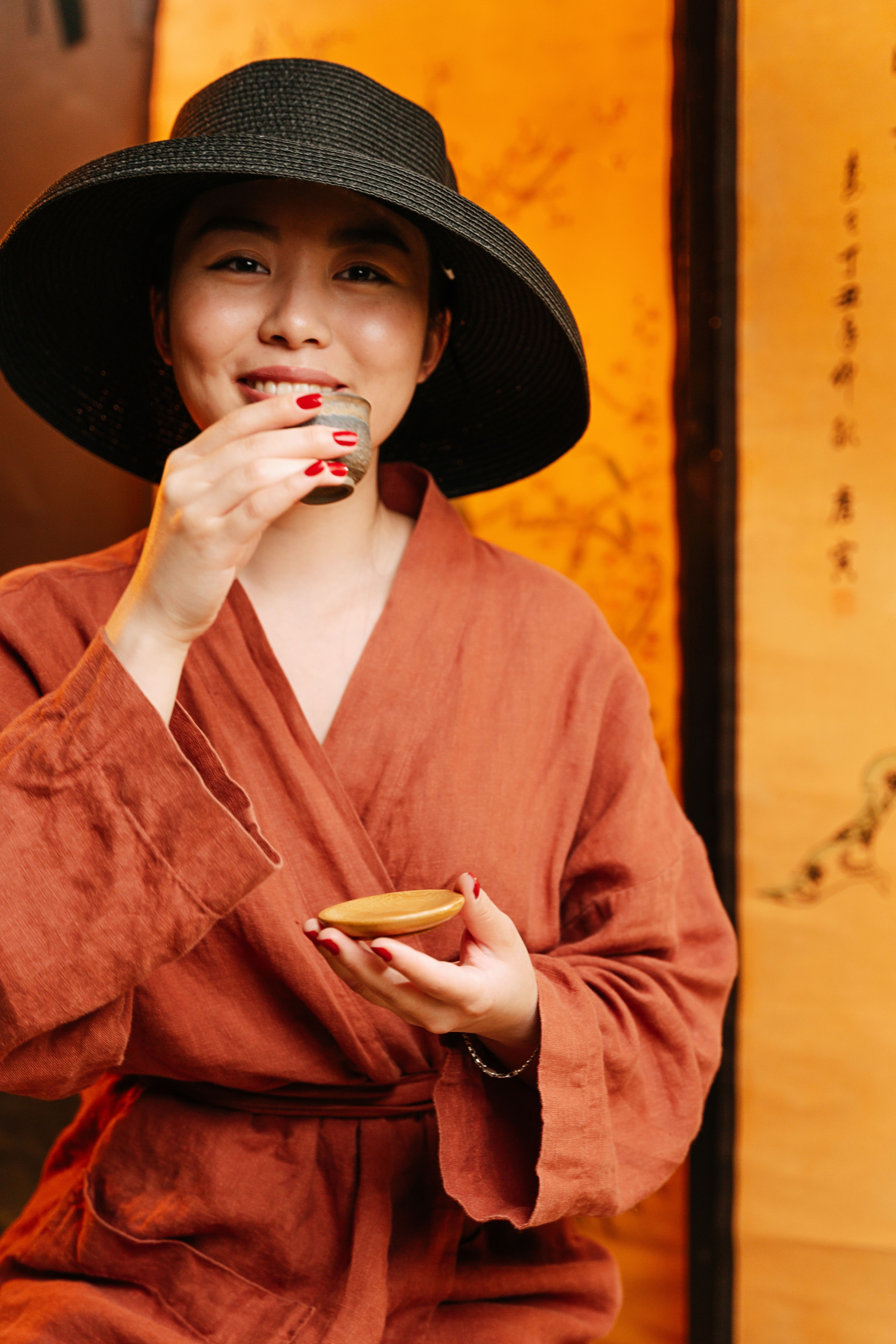A Woman in Black Hat Smiling while Holding a Teacup · Free Stock Photo