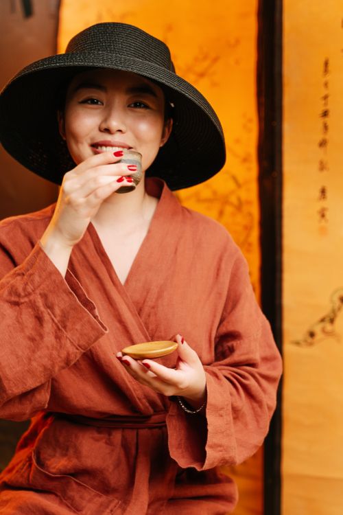 Free East Asian woman in robe and hat enjoying a tea ceremony indoors. Stock Photo