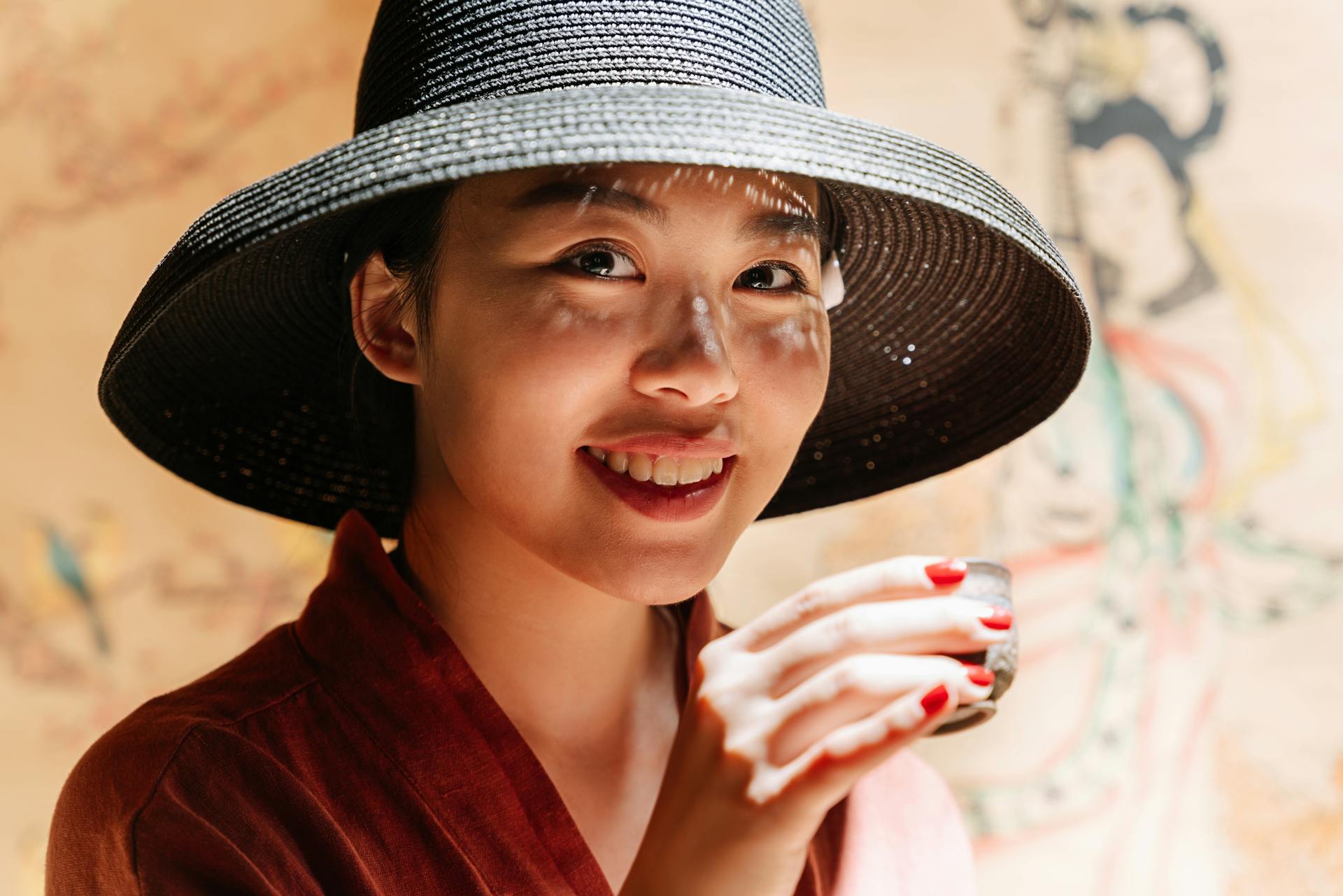 Une femme souriante portant un chapeau noir et tenant une tasse de thé