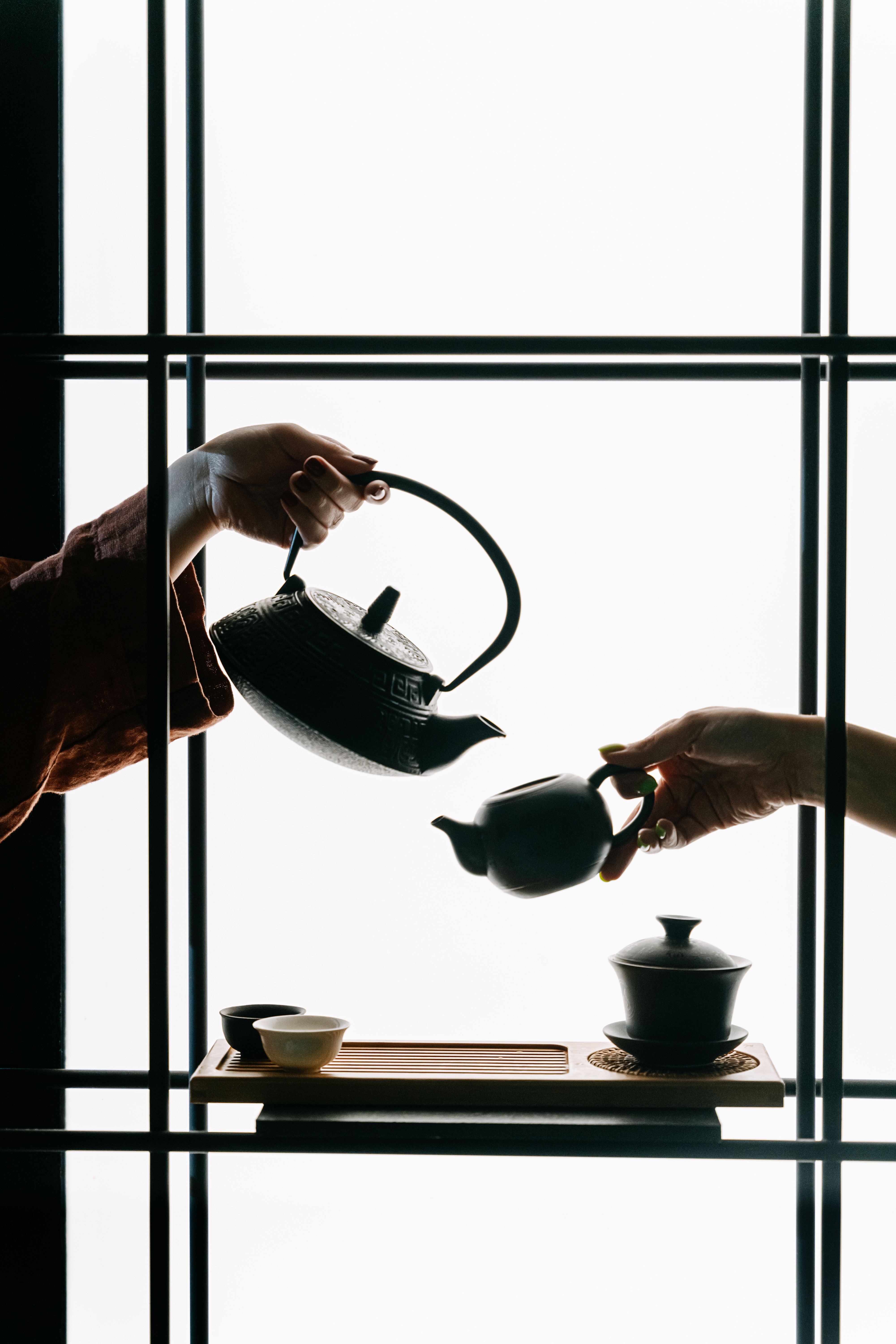 Silhouette of hands performing traditional tea ceremony pouring from cast iron teapot
