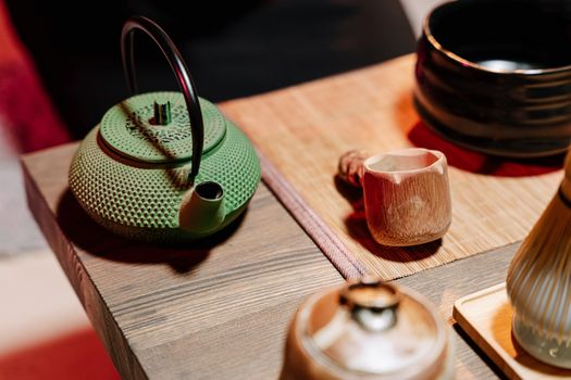A close-up of a traditional tea ceremony setup featuring a green teapot and wooden utensils.