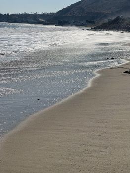 Picturesque scenery of foamy waving ocean washing empty sandy beach in sunny day