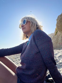 Side profile of a woman sitting on a sunny beach wearing sunglasses.