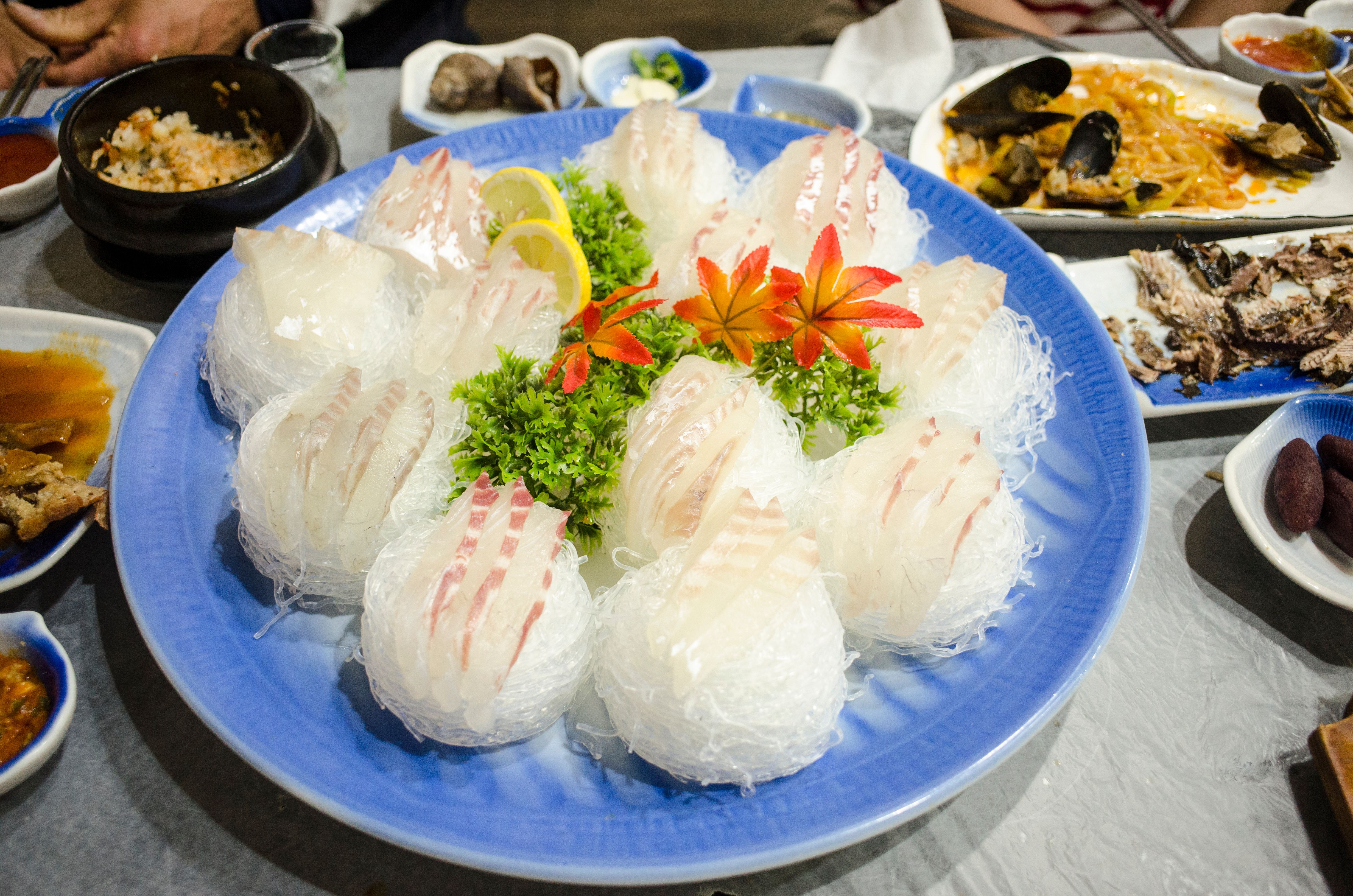 A vibrant dish of sashimi, artfully garnished and served on a blue plate, surrounded by side dishes.